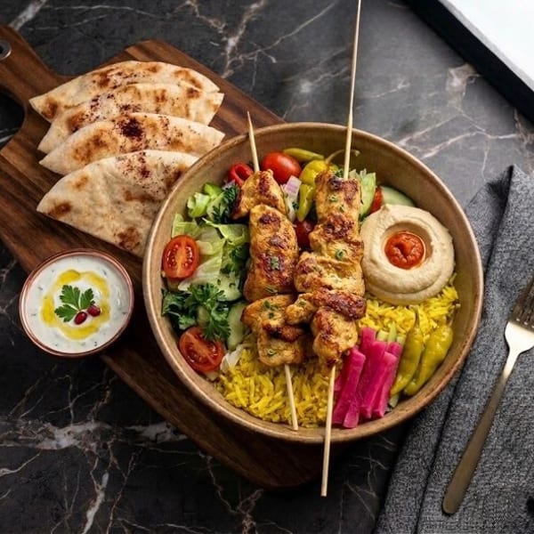 Chicken shish tawook skewers with rice, hummus, salad, pita bread, and tzatziki sauce.