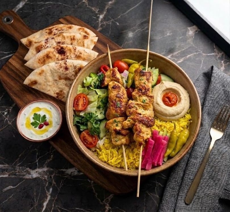 Chicken shish tawook skewers with rice, hummus, salad, pita bread, and tzatziki sauce.